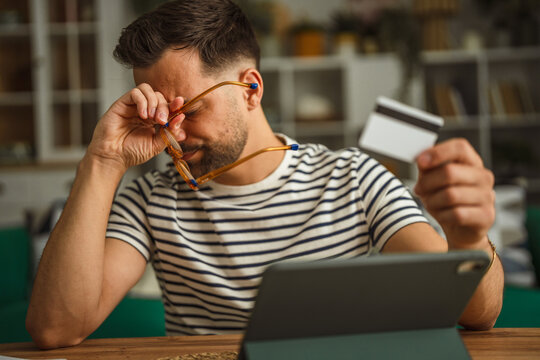Man feeling financial stress holding credit card and rubbing eyes