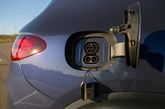 Close up of an open charging port socket on a modern blue electric car or plug-in hybrid vehicle.