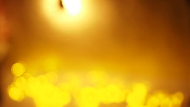 Static close up out of focus shot with warm golden yellow light source. Soft diffused bokeh effect with circular light orbs at bottom of frame. Steady ambient glowing texture against dark background