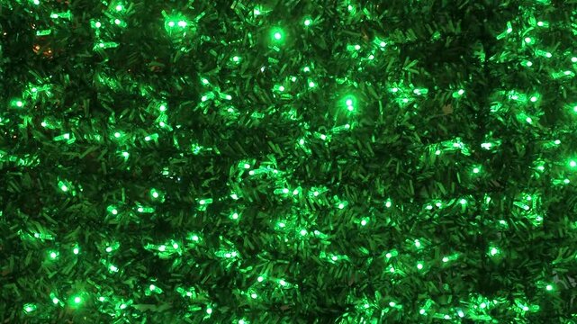 Static close-up of artificial tree foliage covered in dense green LED string lights. Dark textured needles with consistent vibrant green illumination throughout the frame