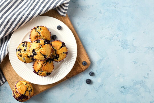 Blueberry muffins on plate over wooden board and blue background