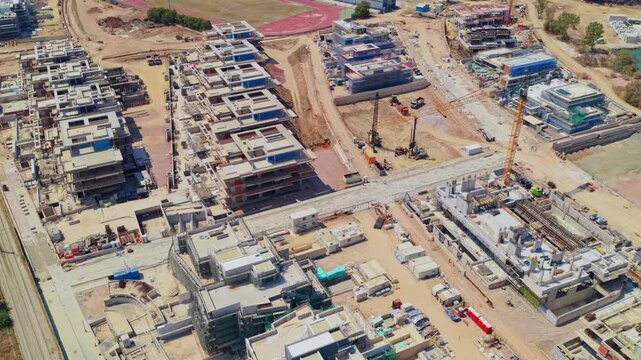 Expansive construction site showing multiple concrete buildings and apartments under development, with heavy machinery and tower cranes operating in a large-scale real estate project