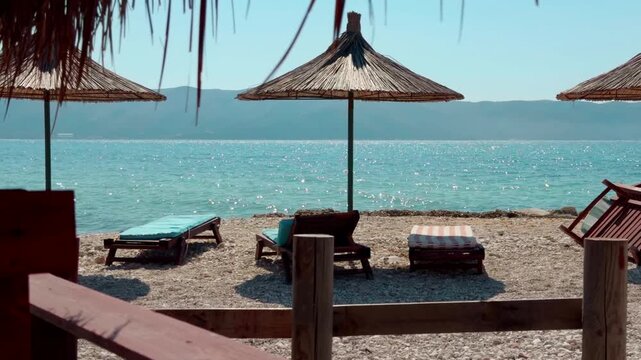 Straw Parasols And Sunbeds On Empty Pebble Beach. Sparkling Sea Waves. Coast Tourist Resort. Summer Vacation Tropical Island 