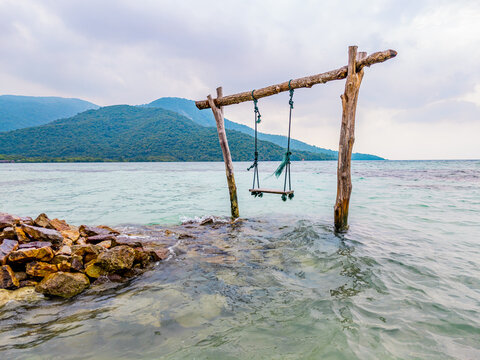 Wooden swing set in the clear shallow water near a rocky beach, offering a peaceful and inviting scene for relaxation and tropical escape in Karimunjawa, Jepara, Indonesia