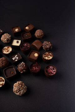 assorted gourmet artisan chocolates and truffles artfully arranged on a dark matte backdrop, moody low-light studio food photography highlighting rich cocoa tones, creamy fillings, nuts, and berry acc