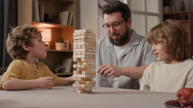 Caucasian middle aged father and two young Caucasian boys playing wooden block tower game at home. Ideal for family bonding, home entertainment, and parenting advertisements