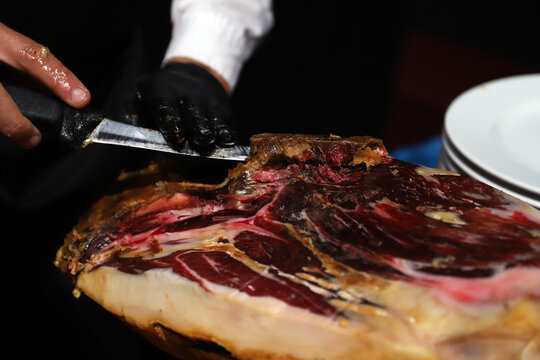 maestro cortador de jam&oacute;n manipulando un jam&oacute;n con guantes y cuchillo jamonero