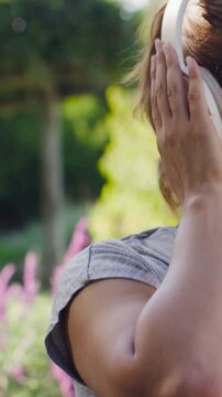 Vertical video: Tapping right earcup grey top woman fitting phones for music in garden, copy space