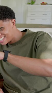 Vertical video: Smiling man on sofa at home wearing olive tee reacting to off-frame voice, laughing