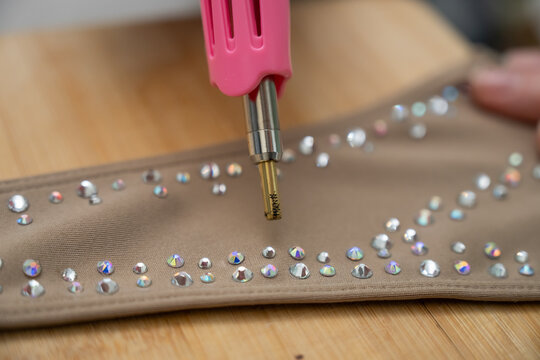 A woman glues rhinestones onto a gymnastics costume using a soldering iron. Hot fix.