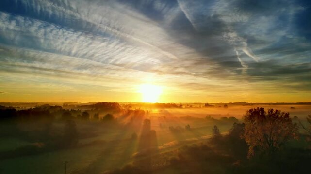 Sunrise over a misty landscape with sunbeams breaking through the clouds.