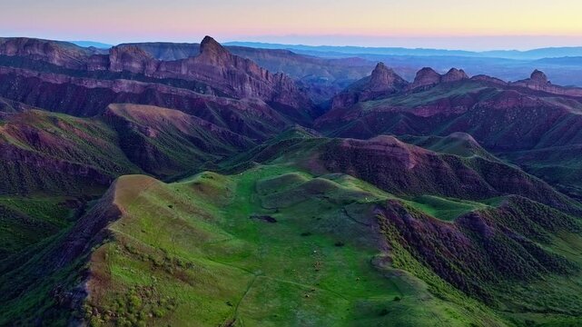 Aerial high angle view of dramatic jagged mountain range and green valley during twilight in Xinjiang, China.