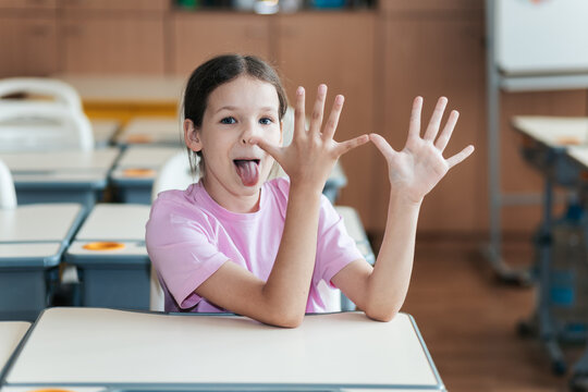 Enjoying the First Day Back at School, a Cheerful Schoolgirl Shows off Her Fingers While Teasing Her Classmates in a Bright Classroom Filled With Excitement