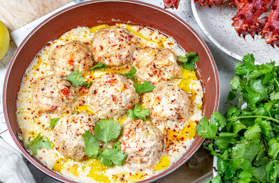 CRABMEATBALLS crab meatballs in white creamy sauce in red pan, whole king crab, cilantro, lemon and white wine on white background