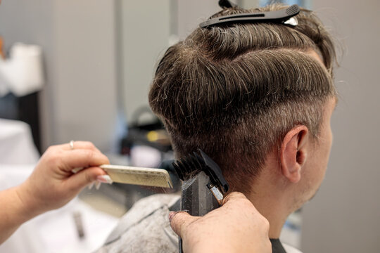 Barber using an electric hair clipper with a hair comb to cut a man hair, creating a professional fade haircut in a modern barbershop salon this quiet afternoon