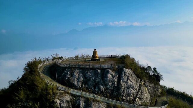 A serene golden statue atop a rugged mountain peak, emerging from a vast sea of clouds under a clear blue sky.