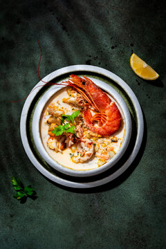 Seafood chowder soup with jumbo prawn, and mussels photographed under hard light. Premium gourmet dish, presented on dark green background with copy space.