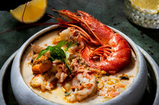 Creamy seafood chowder soup with jumbo prawn, mussels, and parsley in hard light. Close up gourmet seafood delicacy, on dark green background with copy space.