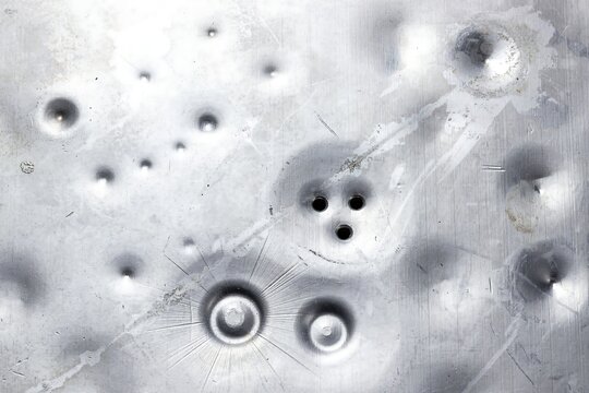 A close up view of a metallic surface with numerous bullet holes and impact craters showing signs of damage and destruction