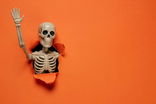 Small plastic skeleton figurine holding a golden key, isolated on orange background, toy skeleton