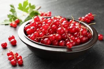 Fresh red currants in bowl and green leaves on dark grey textured table, closeup © New Africa