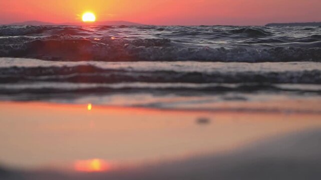 The sun sets over the ocean, casting a warm glow on the water and reflecting on the wet sand.