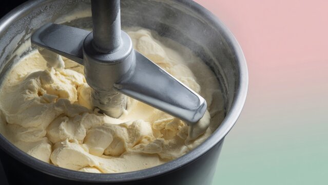 Vanilla ice cream mixture churning in a metal bowl inside a food appliance, creating a creamy dessert