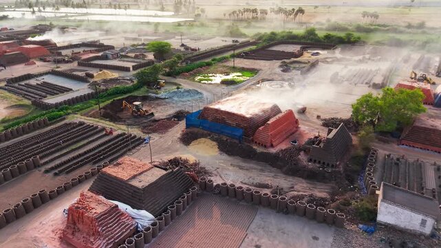 Brick kiln factory releasing smoke while stacks of clay bricks dry in the open yard