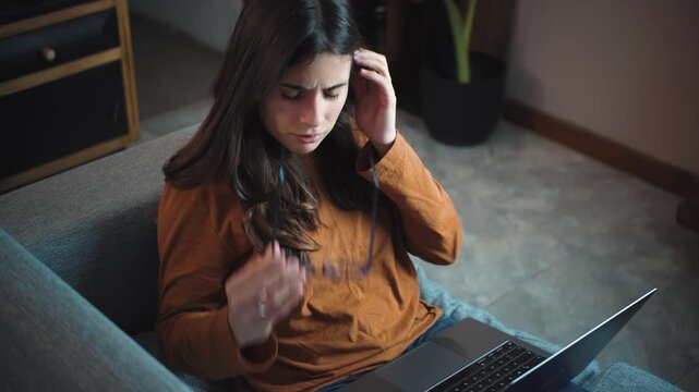 Young Hispanic woman sitting on her sofa with a laptop, experiencing digital eye strain and tired eyes after using a computer for many hours at home.
