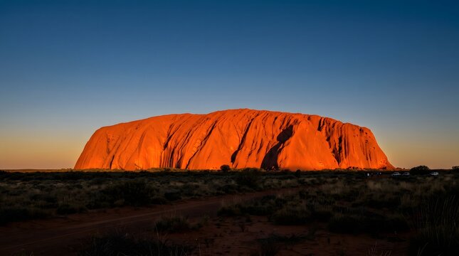 Massive red sandstone monolith rising abruptly from the flat desert outback at sunset