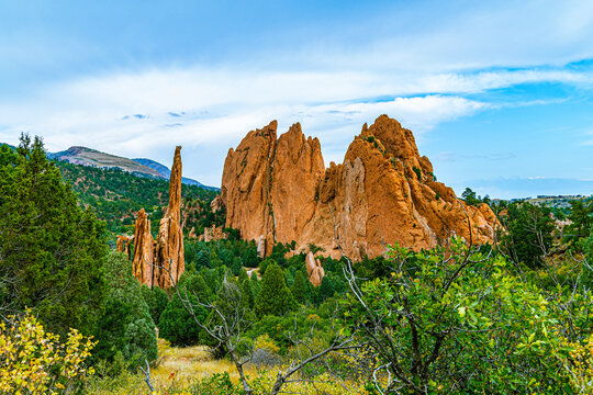 Scenic view of towering red sandstone rock formations framed by green trees under a blue sky in Colorado Springs.