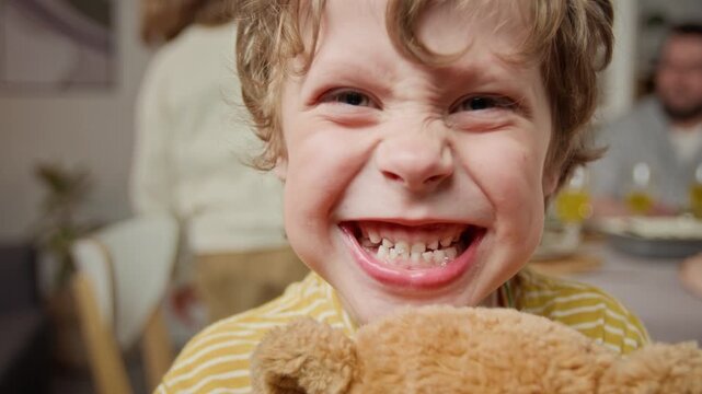 Portrait of Caucasian child boy looking at camera, grimacing and showing teeth while holding plush bear. Ideal for pediatric dentistry marketing, dental hygiene campaigns, or family lifestyle ads