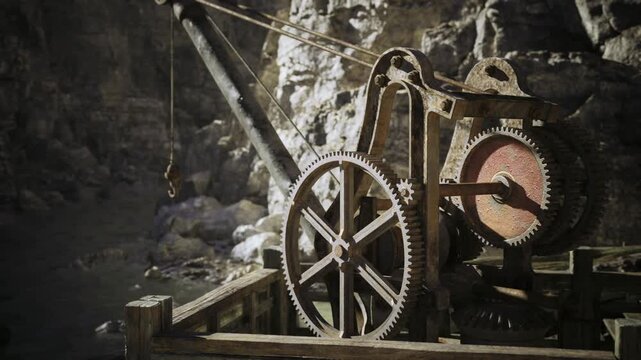Rusty mine winch against rocky slope, Namibia. Corroded gears and pulleys connected by thick cable, rough stone walls and scattered tools, strong directional