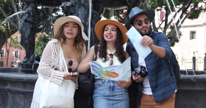 portrait of young latinos friends traveling and holding a tourist map in Mexico downtown in Latin America, hispanic people tourist in fountain in colonial city 