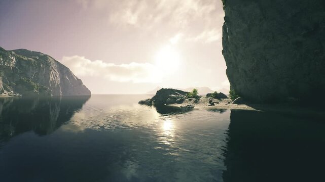 Sunlit rocky cove at sunrise calm glassy water reflecting cliffs and soft clouds, golden light bathing pebble shore, tranquil mood ideal for mindful retreat