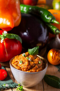 Eggplant caviar in a glass jar and vegetables on a wooden background.
