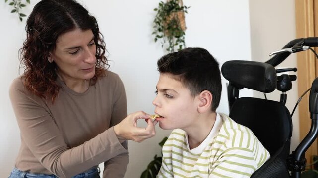 Loving mother feeding disabled son with cerebral palsy