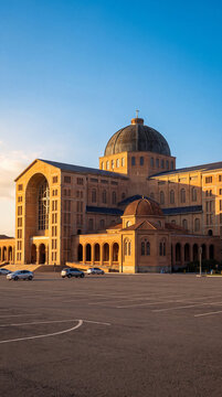 The majestic Cathedral Basilica of Our Lady of Aparecida in Brazil, illuminated by the warm golden light of a late afternoon sun over a large parking lot.