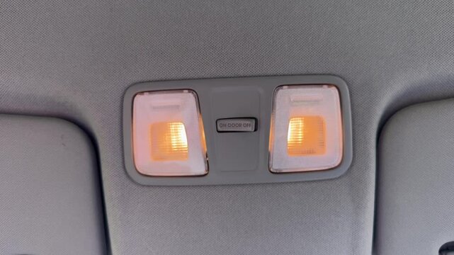  Hand pressing car dome light switch labeled door off on gray ceiling console with illuminated interior lights, automotive interior detail
