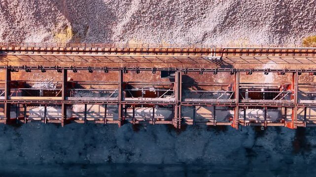 Bulk material handling terminal or industrial loading dock. Drone footage over conveyor belt with moving chutes.