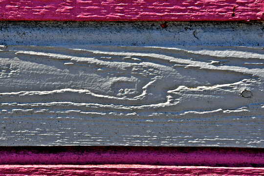 Old painted wood plank with raised grain casting shadows framed by upper and lower pink boarder