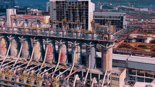 Row of large coke drums at the heavy chemical or oil refinery complex. Drone flight over the huge modern facility near the port.