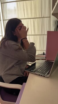 Stressed teenager student working on her laptop getting tired and rubbing her eyes while studying from home in an e-learning session during a stressful time