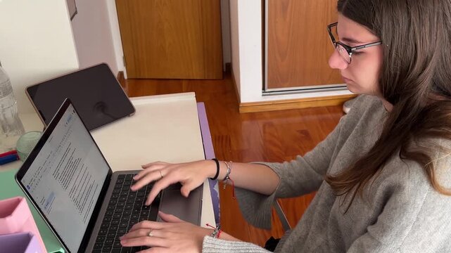 Bored woman sitting at her desk in her room while working online, feeling tired and exhausted during a remote collaborative workday.