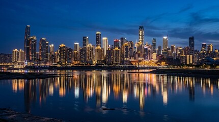 Fototapeta premium Illuminated skyscrapers rise along a river at blue hour with colorful reflections on calm water, suitable for urban travel, real estate, and business marketing.