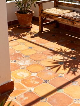 Mediterranean terrace with terracotta tiles and rustic wooden bench. Traditional outdoor patio with potted plant and sunlight shadows. Rustic home decor and architecture