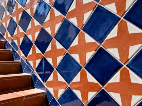 Tiled wall with geometric pattern and terracotta stairs. Traditional Mediterranean ceramic tiles with blue diamonds and orange stars. Close-up of architectural detail in sunlight