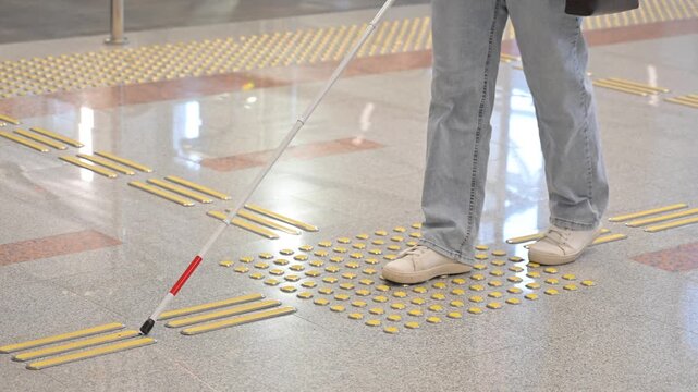 A blind woman walks on tactile paving. Close-up of her feet and a walking stick.