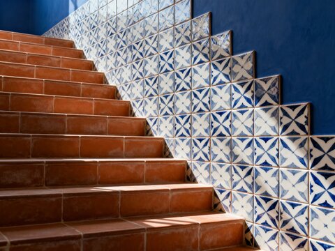 Tiled staircase with terracotta steps and blue patterned wall. Mediterranean interior design with geometric tiles and sunlight shadows. Traditional architecture detail