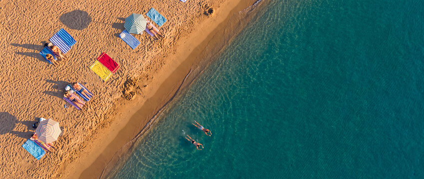 Aerial view of sandy beach and turquoise sea with people sunbathing under umbrellas, featuring golden sand and clear water ideal for summer vacation travel concepts for commercial technology